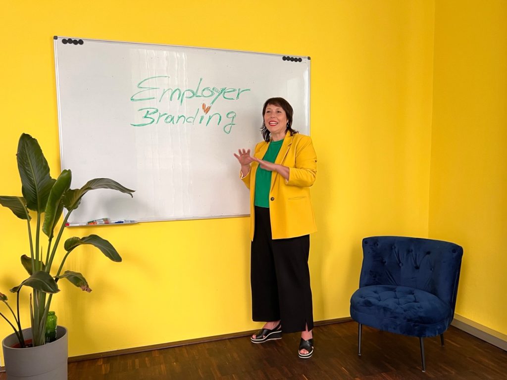 Susanne Gruss erklärt Employer Branding vor einem Whiteboard in einem gelben Raum.